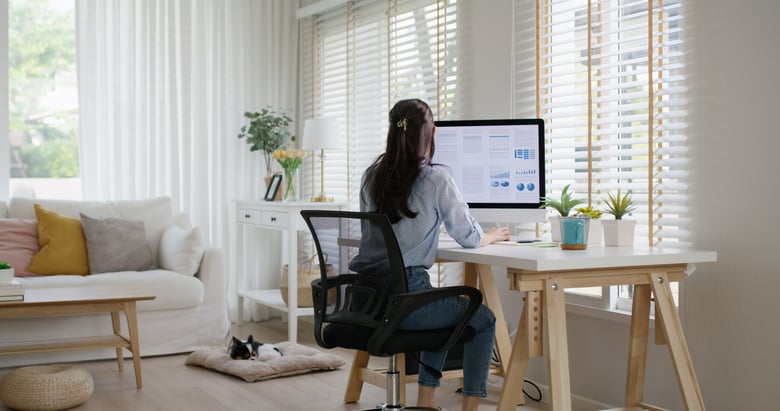 Modern office space reflecting a hybrid work environment. On one side, a sleek desk with a laptop sits in a bright, open area filled with greenery, symbolizing remote work. The other side showcases a traditional conference room with a large table surrounded by ergonomic chairs, equipped with a digital screen displaying a team video call. A calendar on the wall highlights various leave dates, while sticky notes with reminders and policies are affixed to a nearby whiteboard. A coffee station in the corner adds a casual touch, promoting collaboration. Sunlight streams through large windows, illuminating the space and creating an inviting atmosphere. In the foreground, a diverse group of employees—some in business attire and others in casual wear—engage with their devices, embodying the blend of in-office and remote work that characterizes the modern workforce.